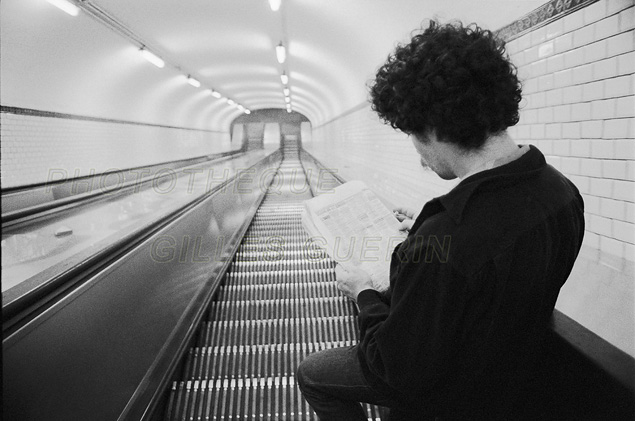 Jeune homme lisant les annonces du journal dans un escalier mcanique du mtro parisien - 1979