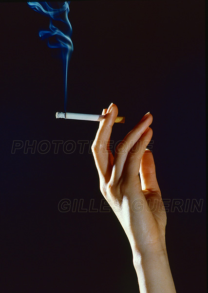 Jolie main de femme tenant un cigarette allume entre le majeur et l'index et volutes de fume bleute